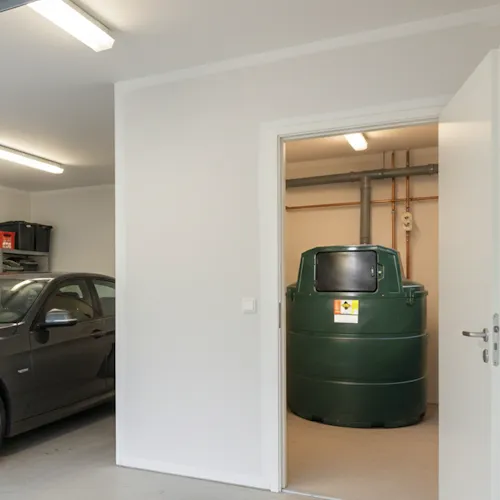 Installation d'une cuve à mazout de 2350 litres dans une chaufferie adjacente au garage, vue à travers une porte ouverte.